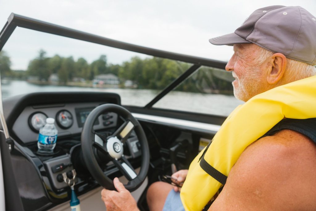 A smiling man wearing a yellow lifejacket drives a boat, buy a boat concept. 