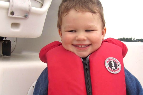 A child wears a red life jacket while smiling on a boat. 