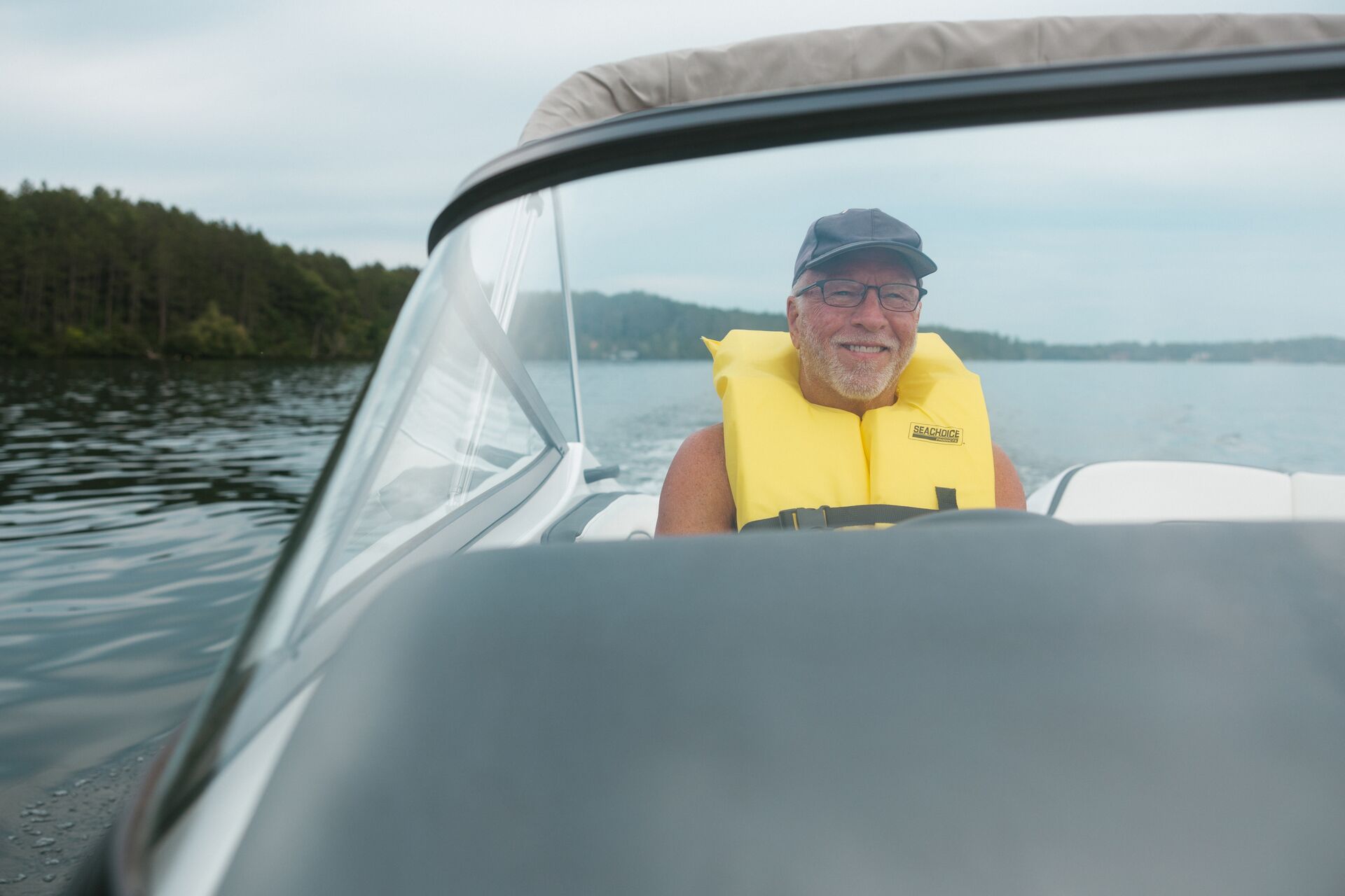 A man driving a boat while smiling and wearing a life jacket, follow New Jersey boating laws concept. 