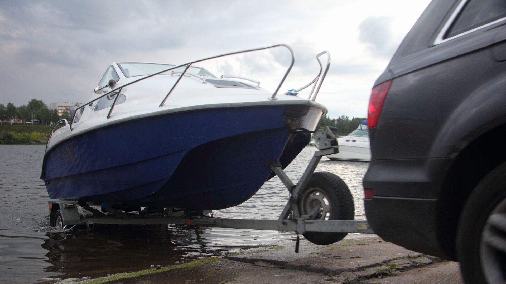 An SUV backing a boat on a trailer into the water. 