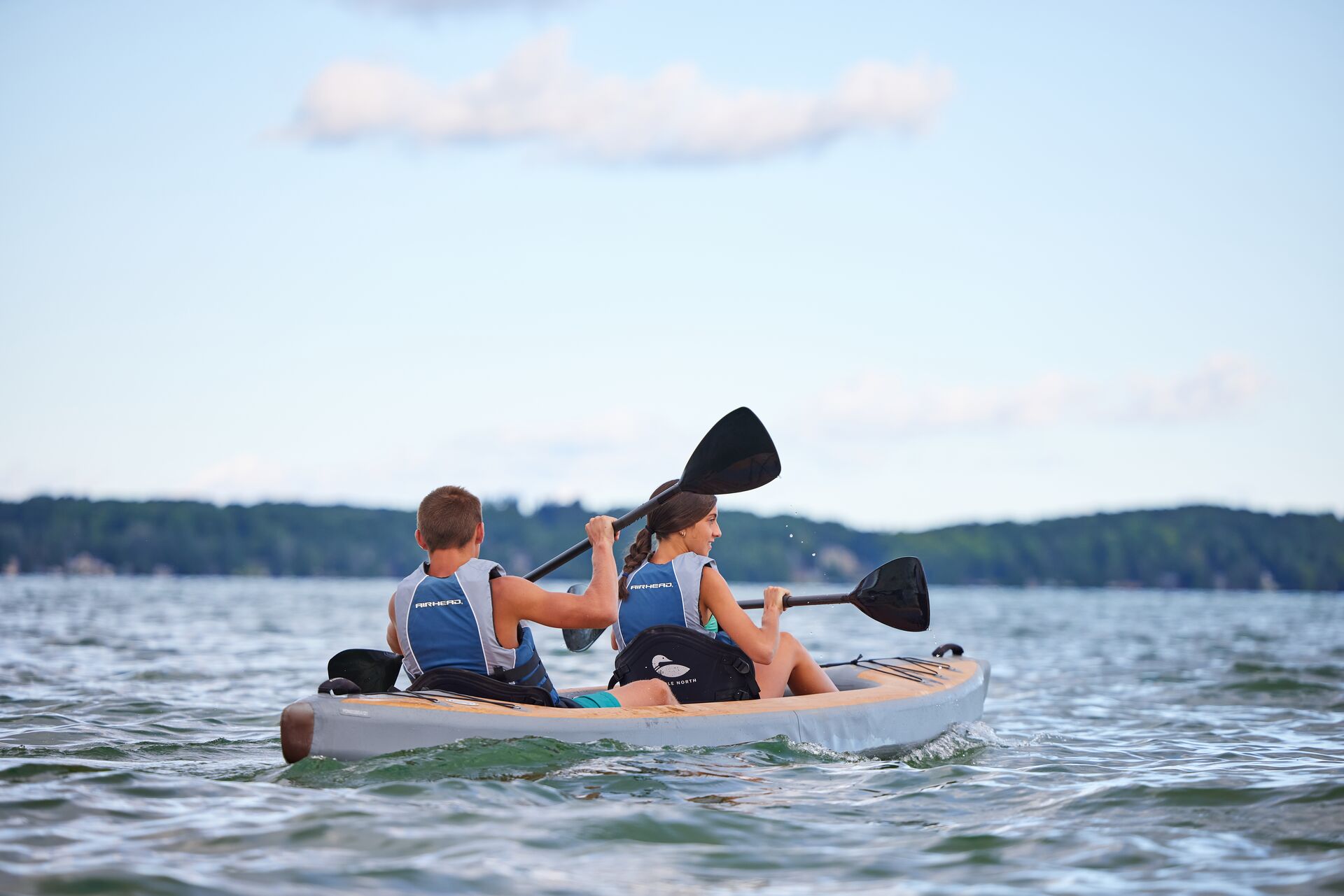 Two kids on the water in a kayak while paddling and wearing life jackets. 