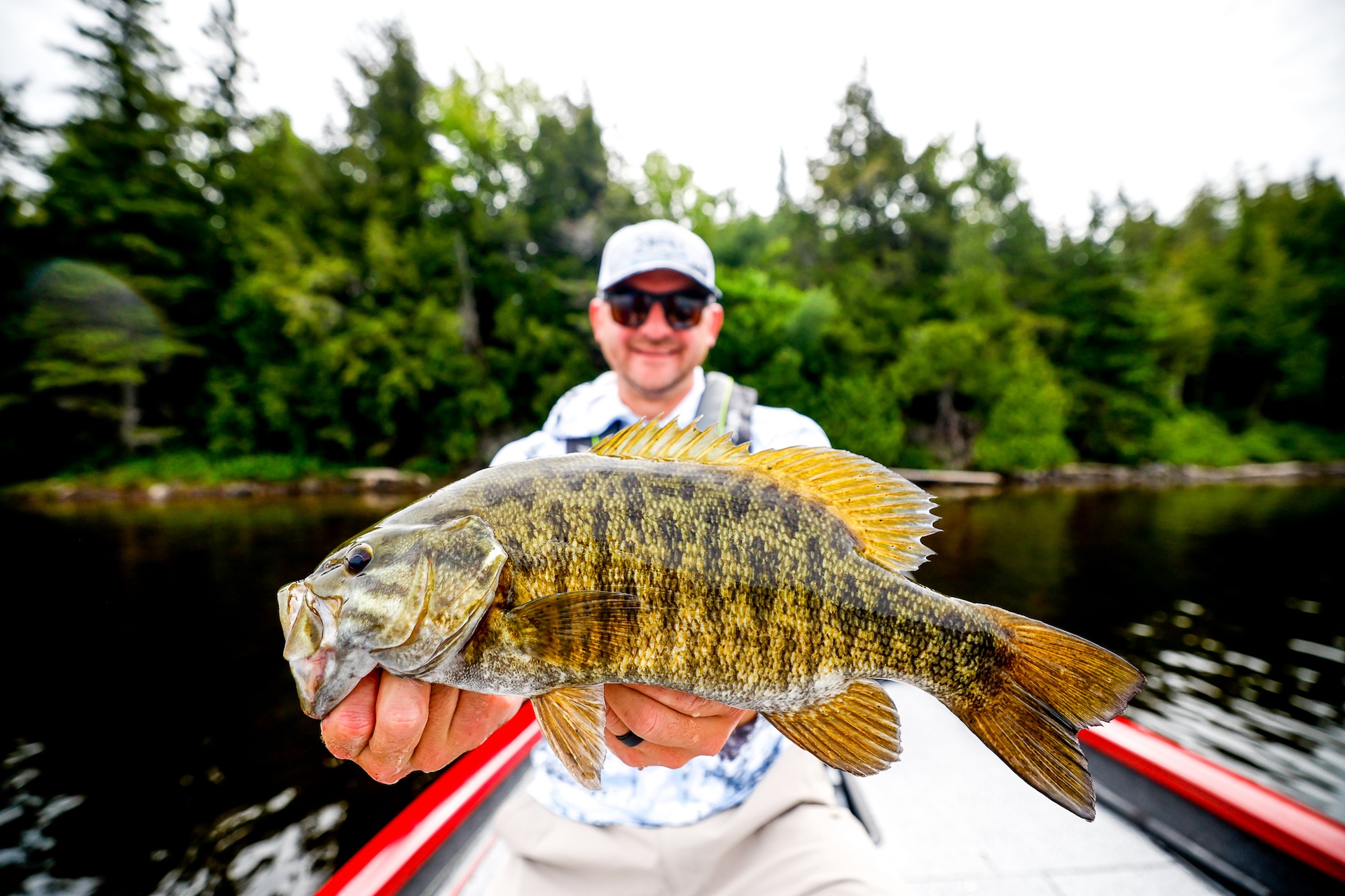 A man in a boat holds up a fish he just caught, fall fishing concept. 