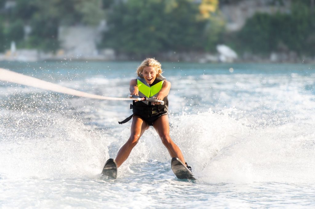 A girl smiling while wearing a life jacket on waterskis on the water. 