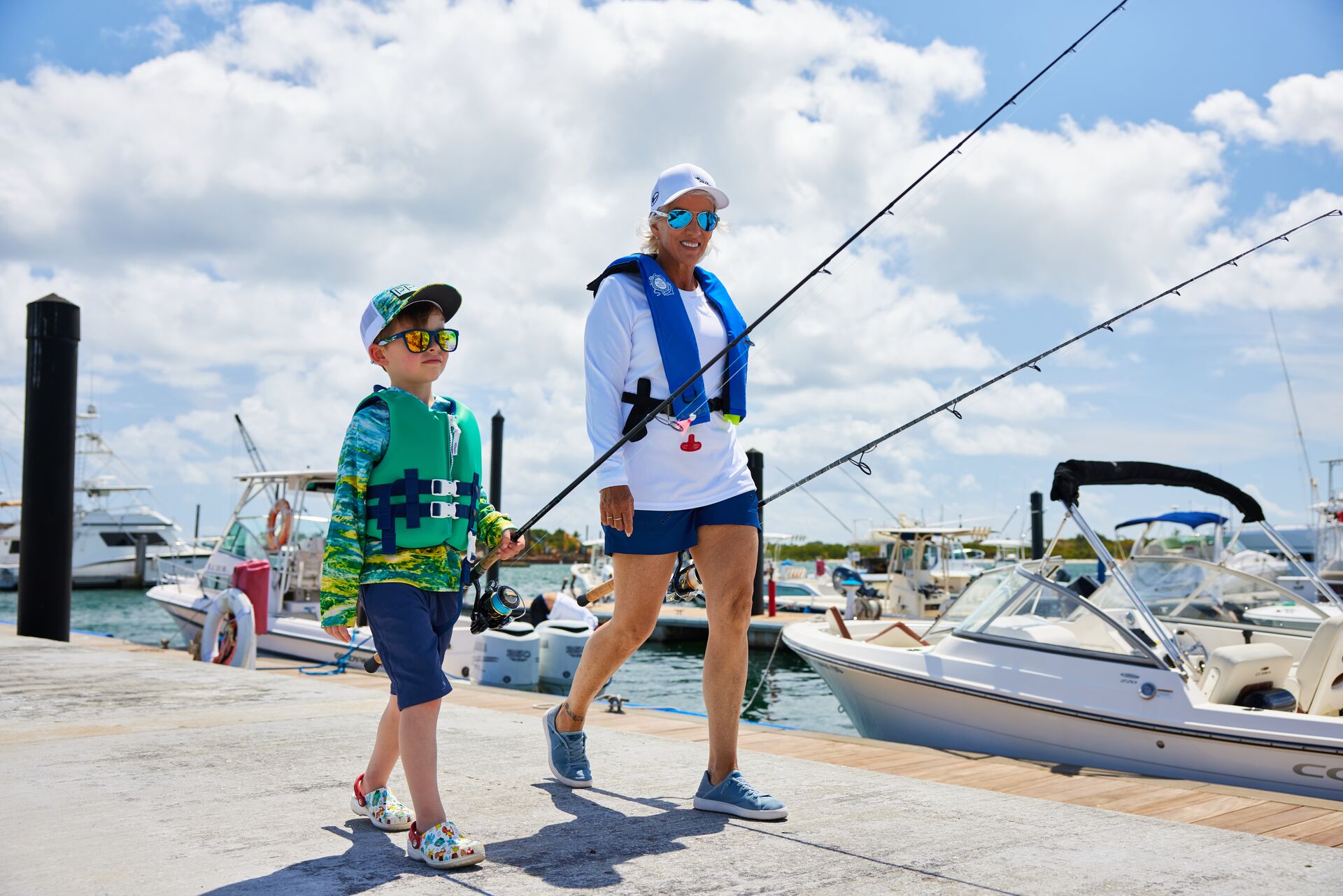 A woman and boy in life jackets walking with fishing poles. 