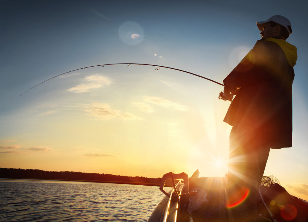 A man with a fishing rod on a boat at sunrise. 