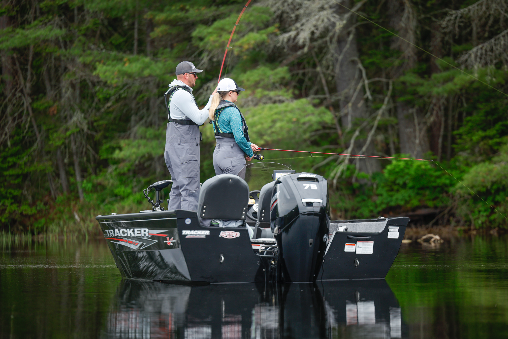 Two people on a fishing boat on a lake with lines in the water. 