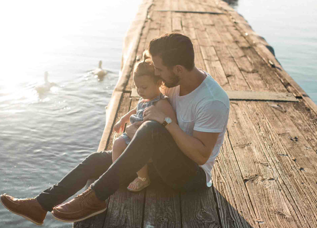 Man and small girl sit on a dock. 