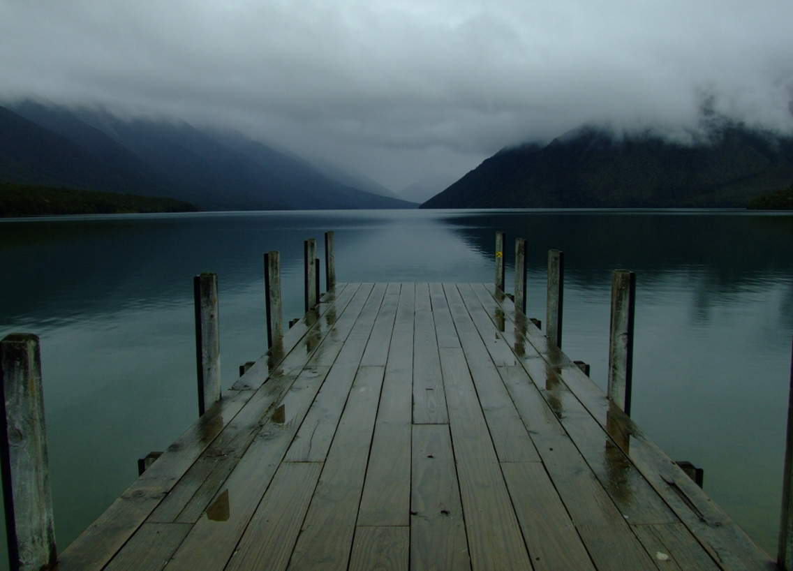 A dock on a lake with clouds and mountains in the background. 