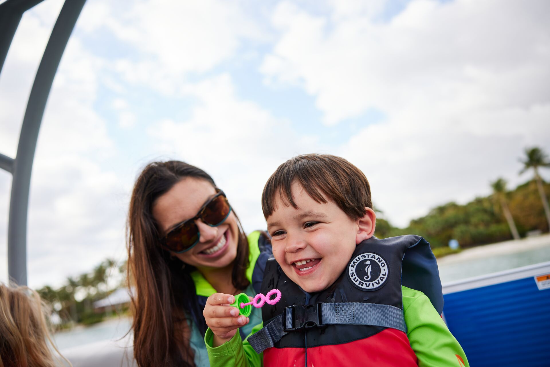 A child and woman smiling while wearing life jackets on a boat. 