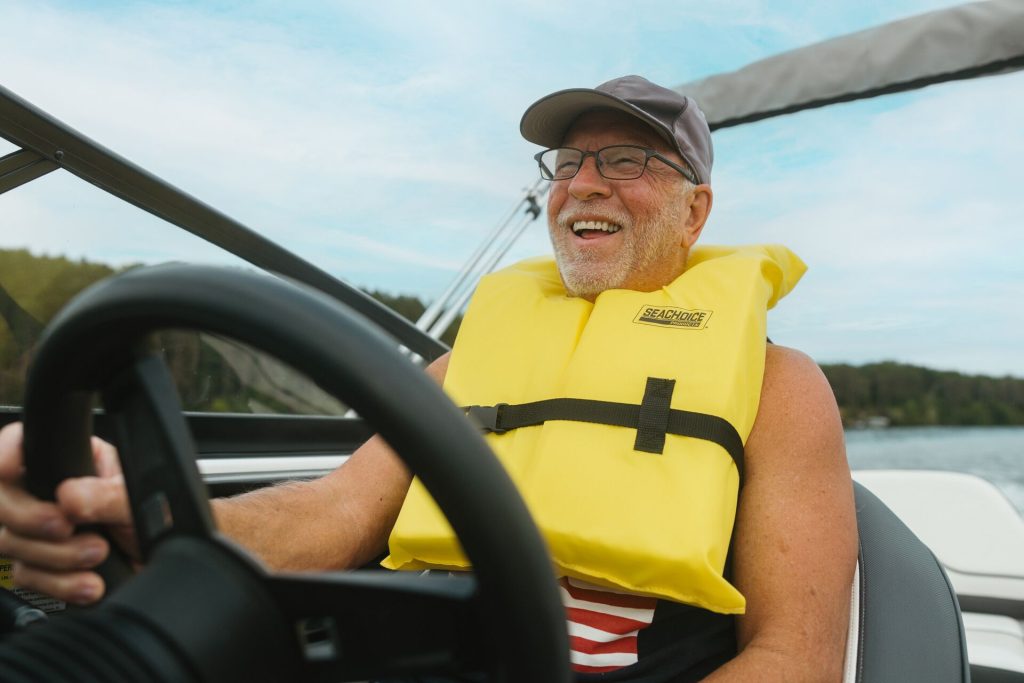 A happy, smiling man wearing a life jacket while driving a boat. 