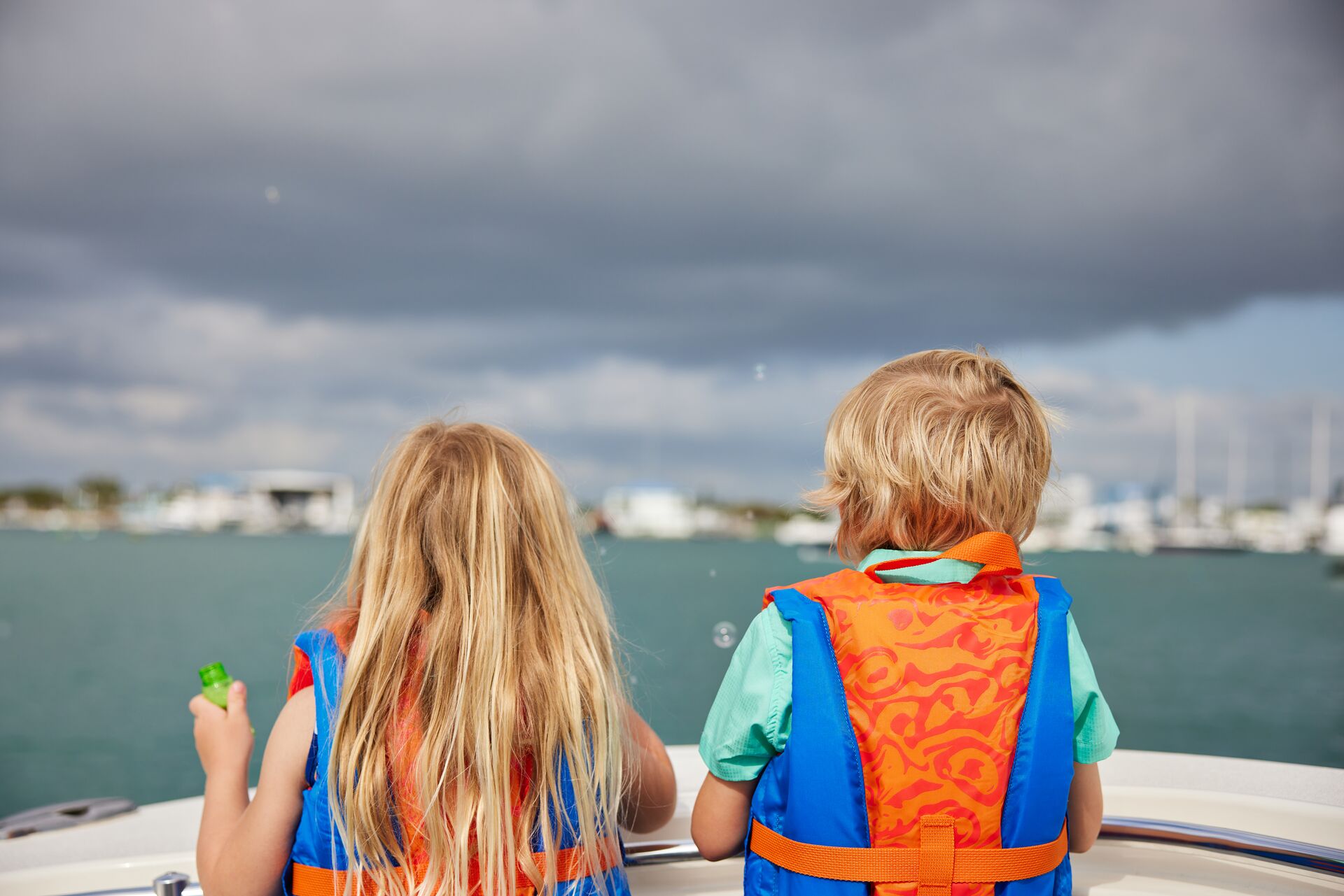 Two children look over the edge of a boat while wearing life jackets, follow Rhode Island boating laws concept. 