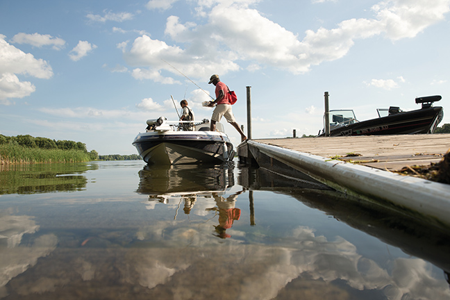 People stepping from a dock onto a boat with fishing rods. 