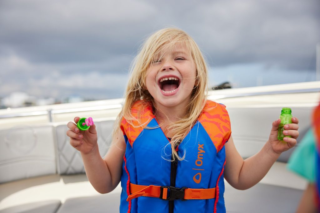 A smiling child wears a personal flotation device on a boat. 