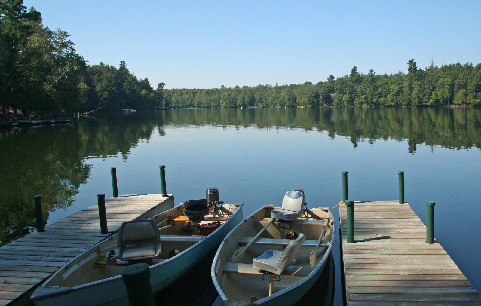 Two small boats at two docks on a lake with trees along the shore. 