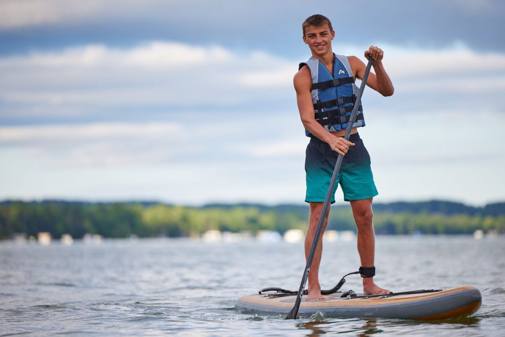 A guy smiling on a paddleboard while wearing a life jacket. 