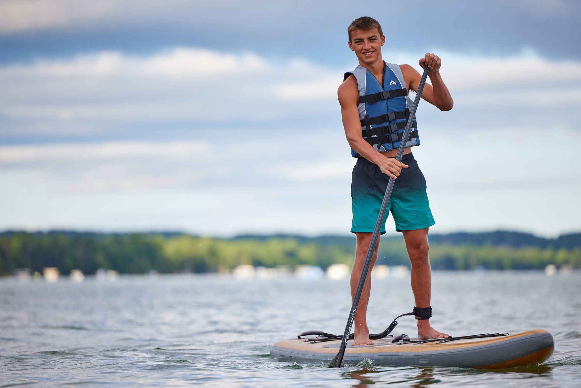 A boy stands on a paddle board while wearing a life jacket. 