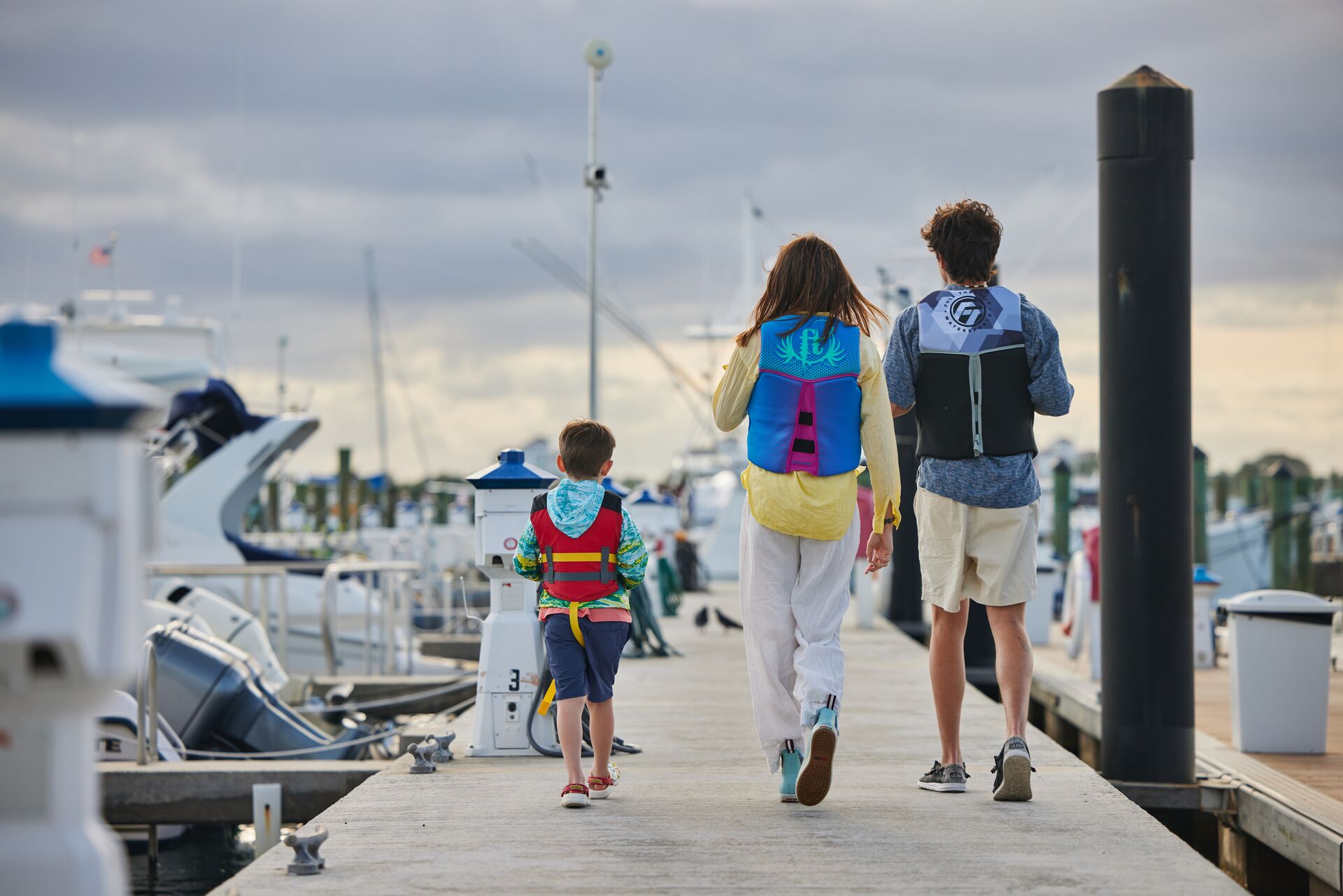 Three kids walking on a marina wearing life jackets, follow New Hampshire boating regulations concept. 