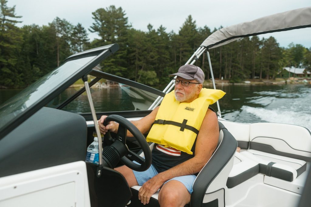 A man wearing a yellow life jacket while driving a boat 