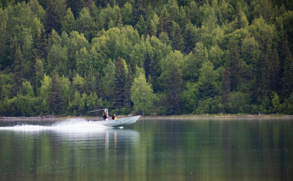 A boat moving across a lake with tres in the background. 