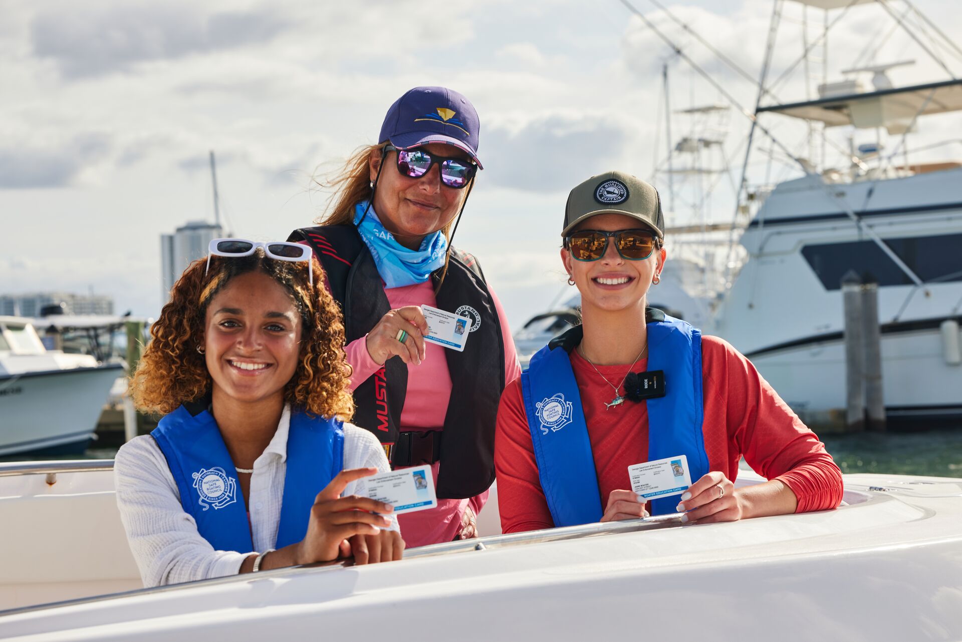 Smiling ladies in lifejackets hold boating license cards.