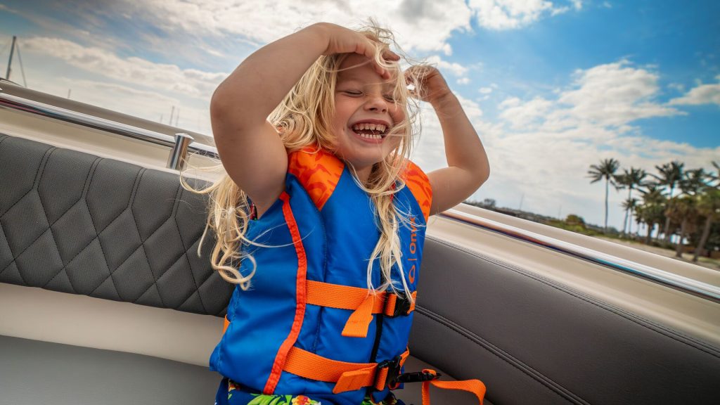 A child wears a lifejacket and smiles on a boat. 