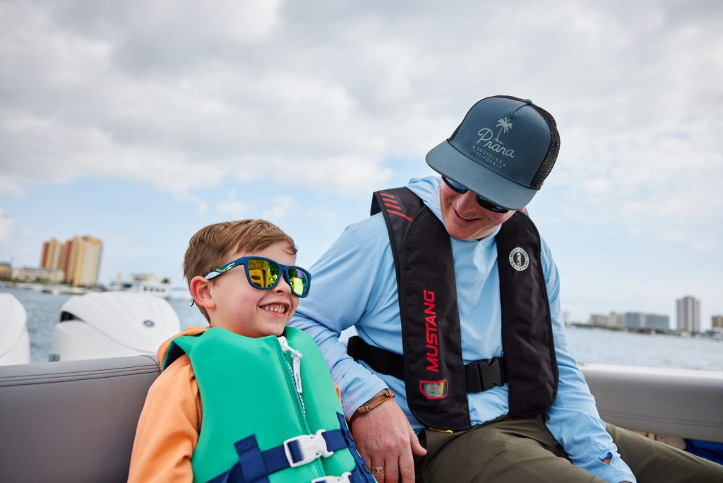 A man and boy smiling while on a boat and wearing life jackets, boating in Virginia concept. 