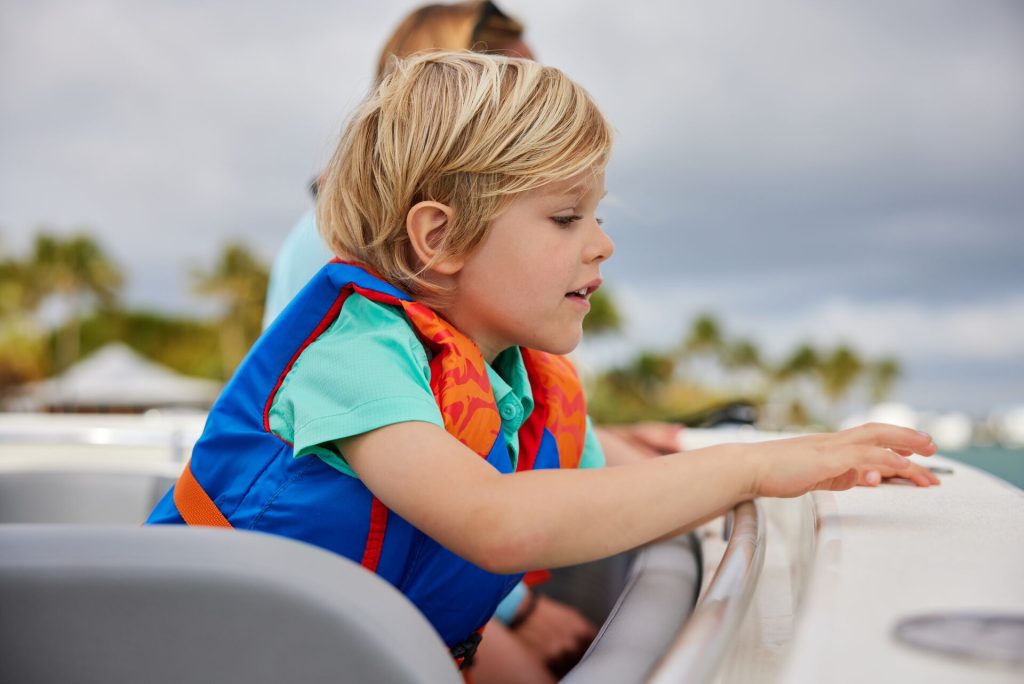 A child looking over the edge of a boat while wearing a life jacket, life jacket laws concept.