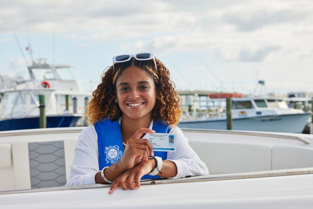 A smiling woman on a boat holds a boater education card, California boater card concept. 