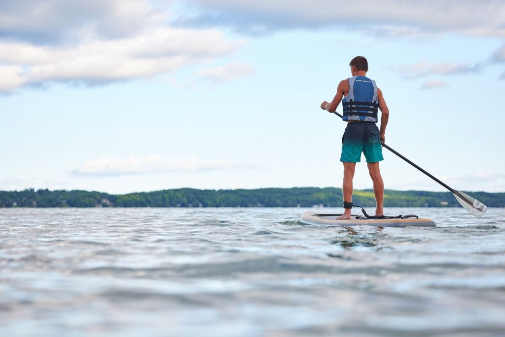 A boy on a paddle board while enjoying the water and wearing a life jacket. 