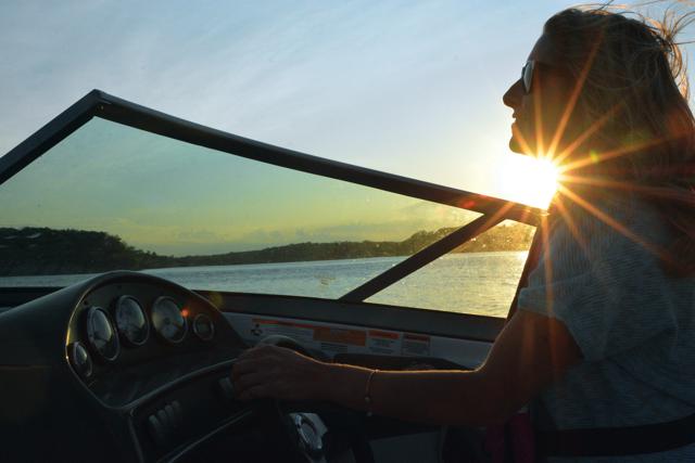 A woman silhouetted driving a boat, don't drink and drive a boat concept.