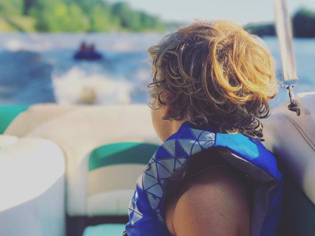 A child wearing a life jacket on a boat watches behind the boat, Louisiana boating concept.